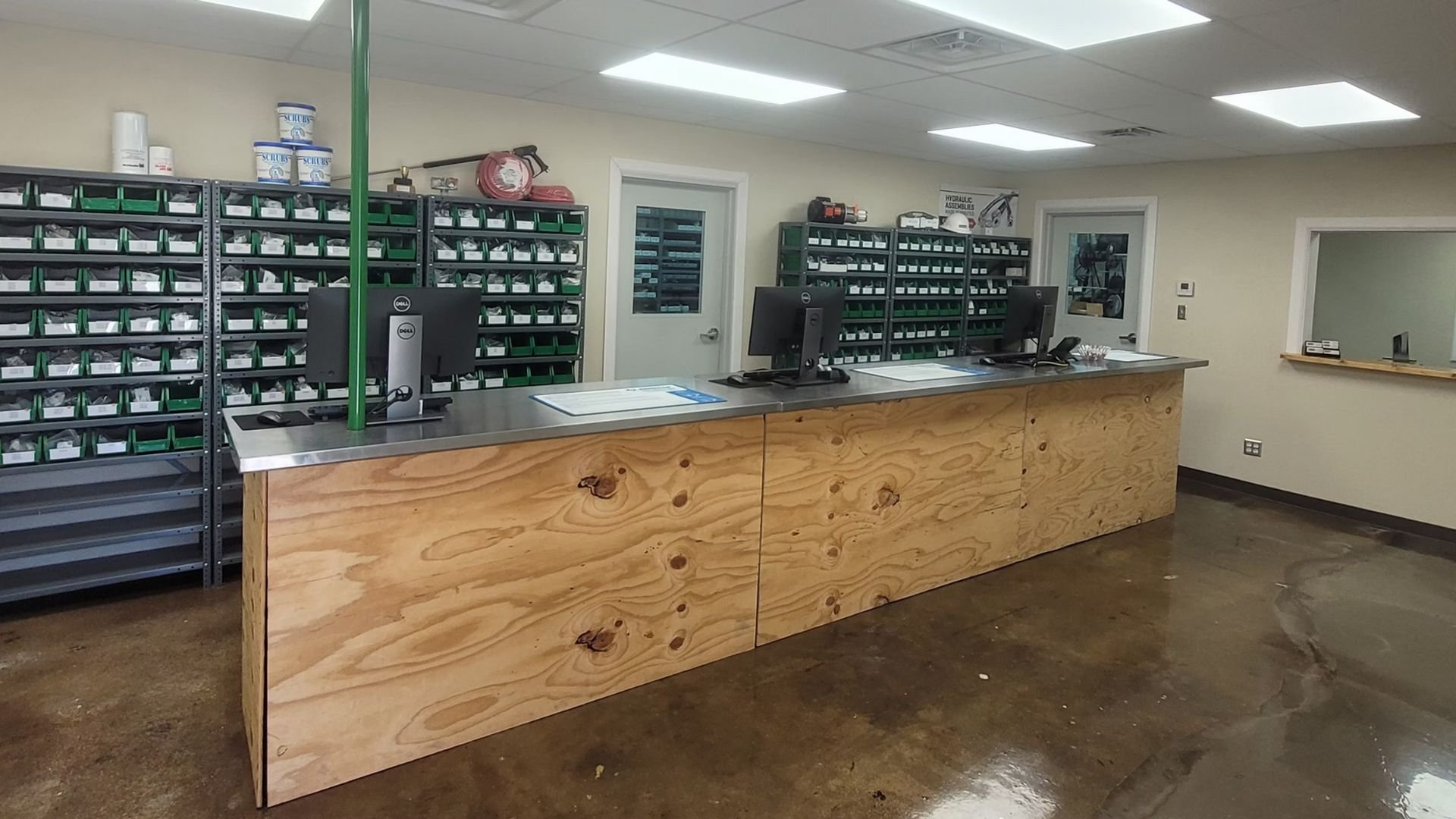 Pharmacy storage room with wooden counter, shelves of green bins, and computers